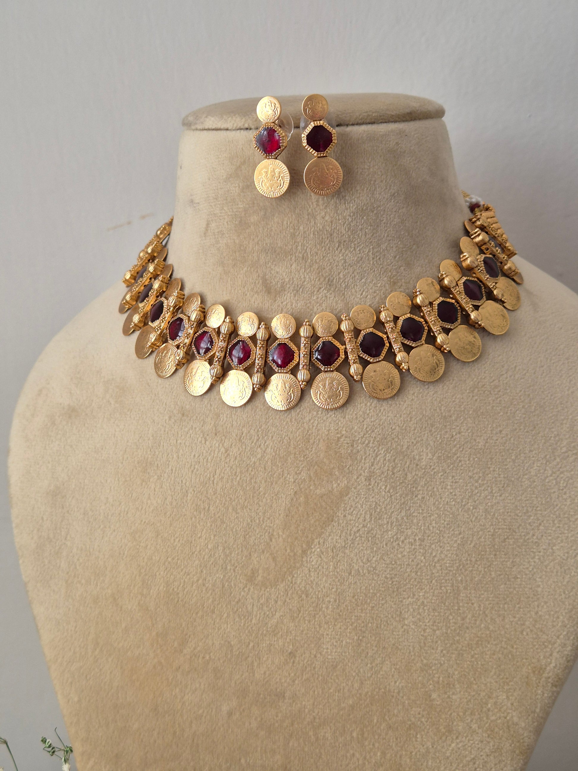 Artisanal  and earring set in a modern Indian aesthetic, Gold-plated brass choker with red stone embellishments, a dangling coin fringe, and coordinating festive stud earrings by naitri.in