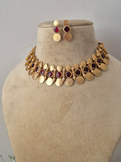 Artisanal  and earring set in a modern Indian aesthetic, Gold-plated brass choker with red stone embellishments, a dangling coin fringe, and coordinating festive stud earrings by naitri.in
