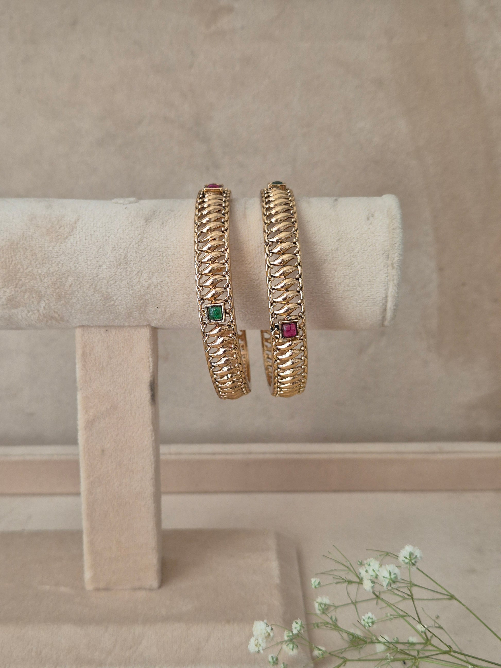 Two gold-toned textured bangle bracelets with small red and green gemstone accents, by naitri.in