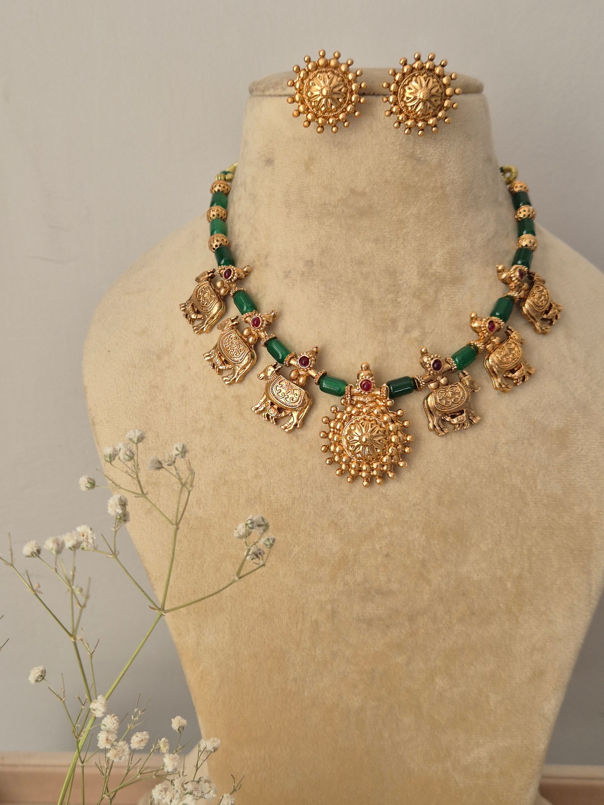 Handcrafted Indian ethnic necklace set with gold-toned mother ccow charms and green bead spacers, featuring a large circular pendant and matching textured stud earring  by naitri.in