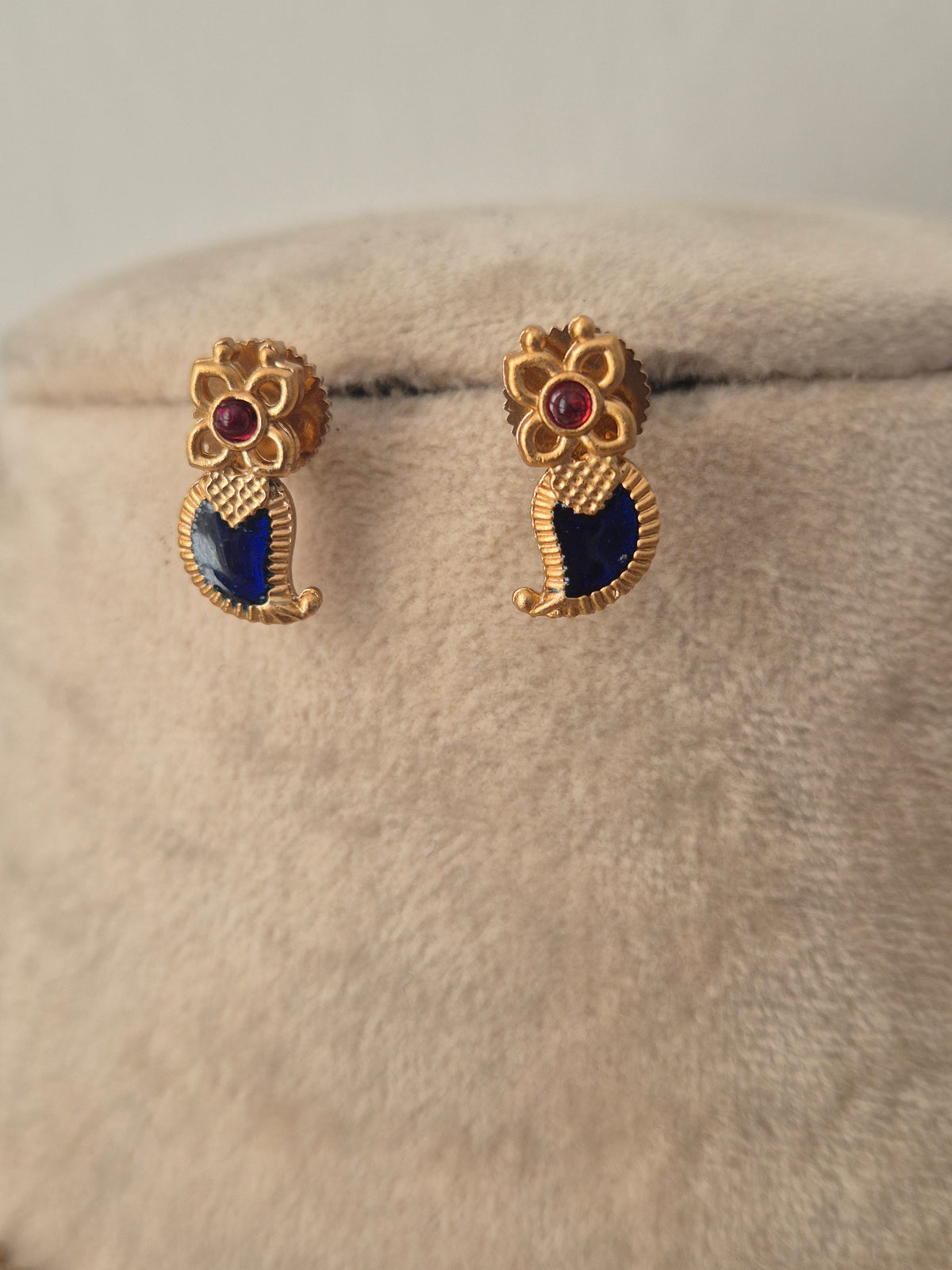 A pair of gold-toned traditional earrings with dark blue enamel paisley motifs and small red gemstone accents, by naitri.in