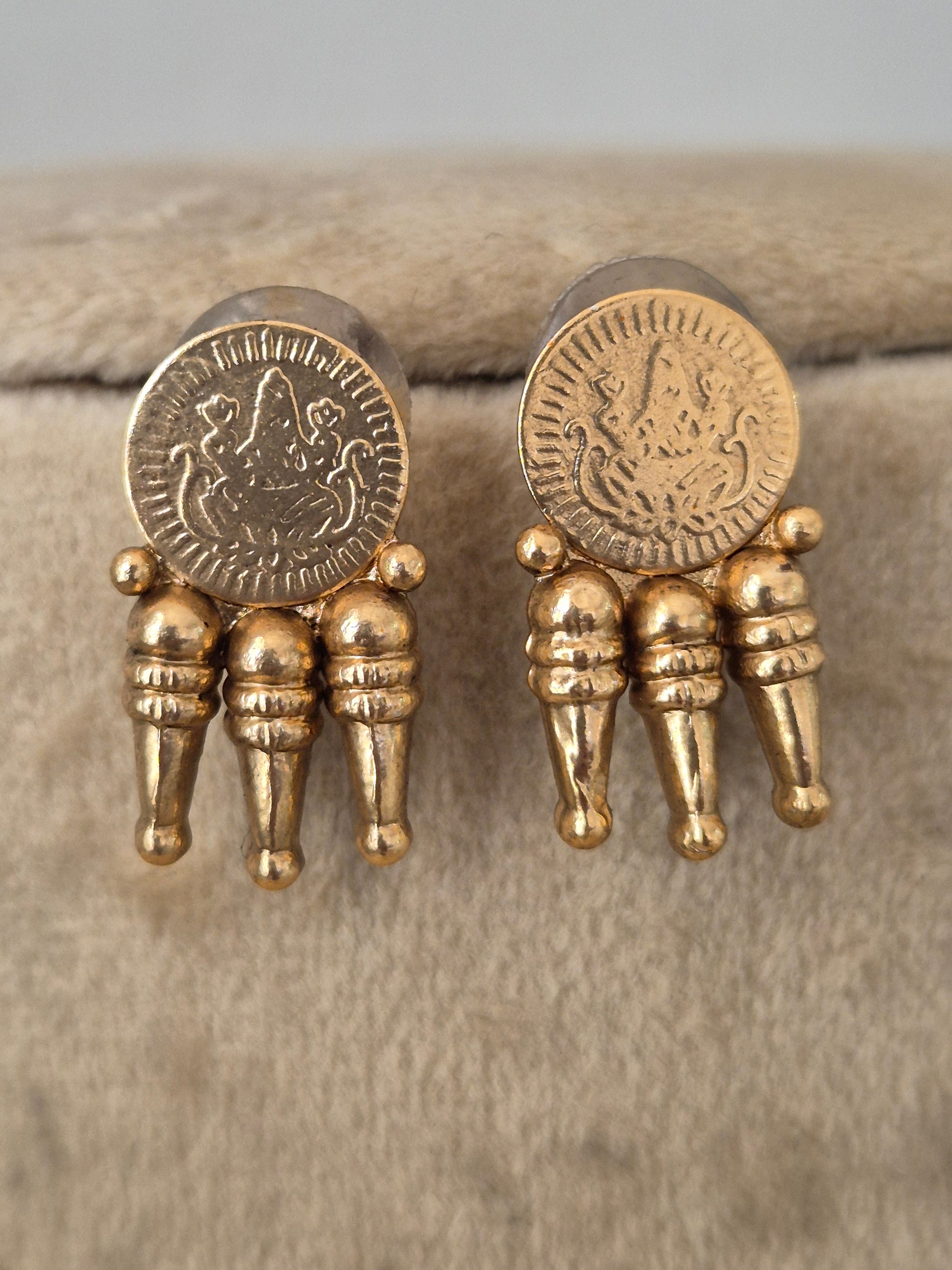 A pair of gold-toned earrings each earring features a circular coin-like medallion with an embossed figure, connected to three small cylindrical gold elements by naitri.in