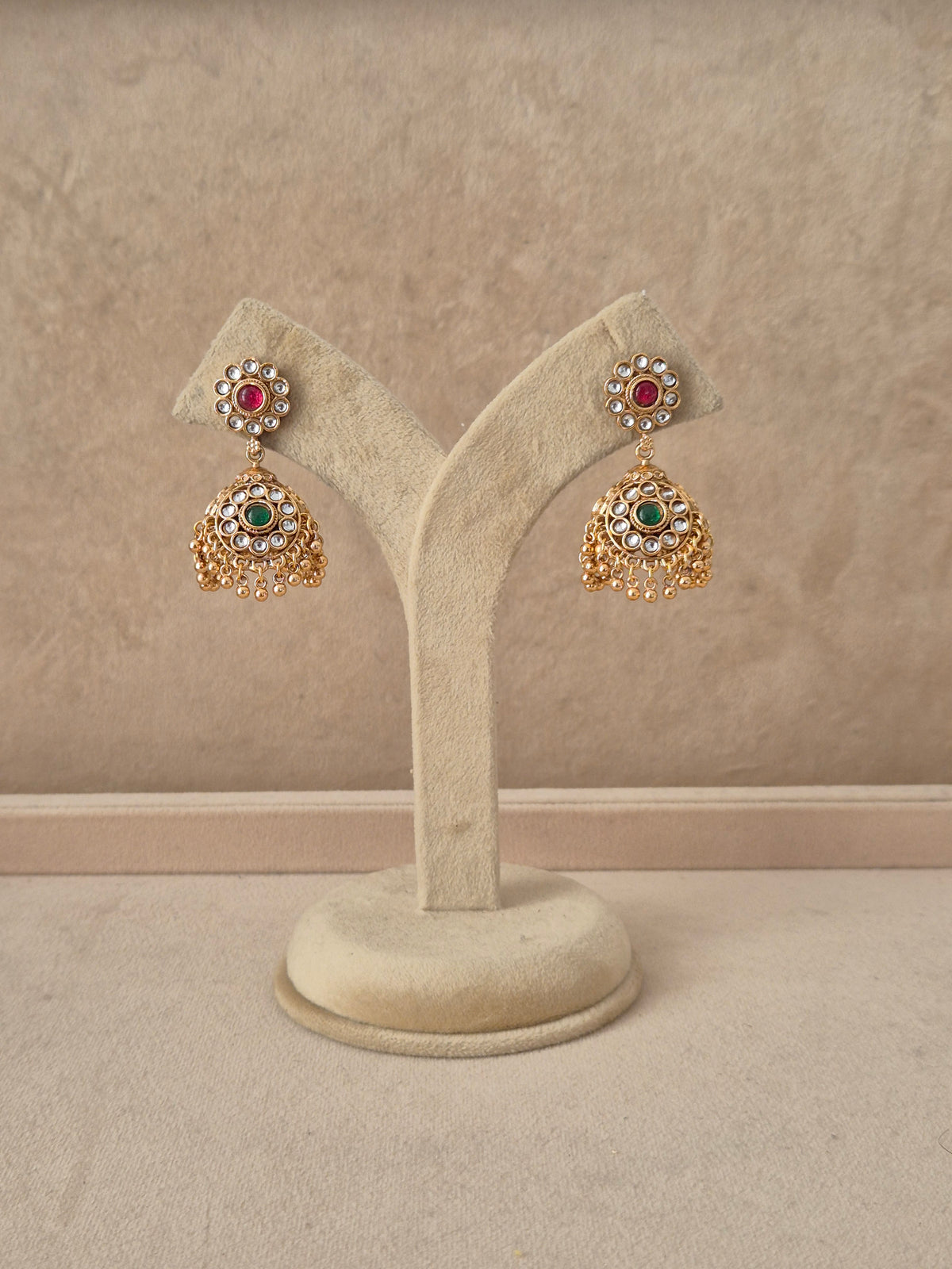 Gold-plated traditional jhumka earrings featuring a circular floral stud studded with ruby-red and emerald-green stones, with tiny pearl drops by naitri.in