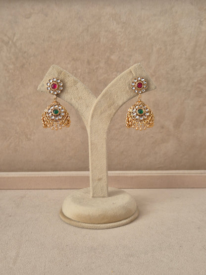 Gold-plated traditional jhumka earrings featuring a circular floral stud studded with ruby-red and emerald-green stones, with tiny pearl drops by naitri.in