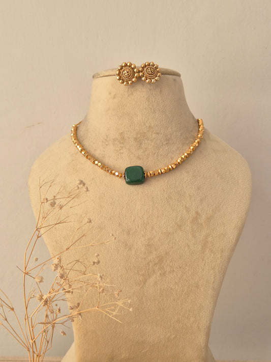 Ishana Green Stone Choker Set displayed on a beige mannequin bust, featuring a delicate golden bead chain centered with a striking square emerald green stone pendant and matching textured stud earrings