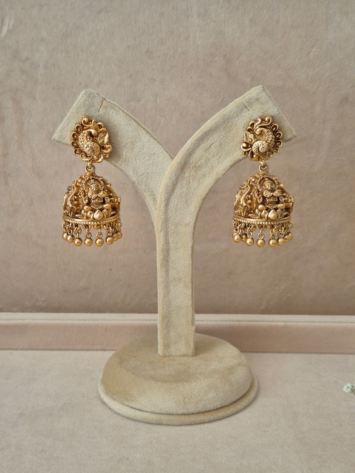 Pair of gold-plated Ishita dangle earrings hanging on a beige velvet display stand, featuring circular studs densely clustered with small white seed pearls and elegant hanging pearl drops by naitri.in