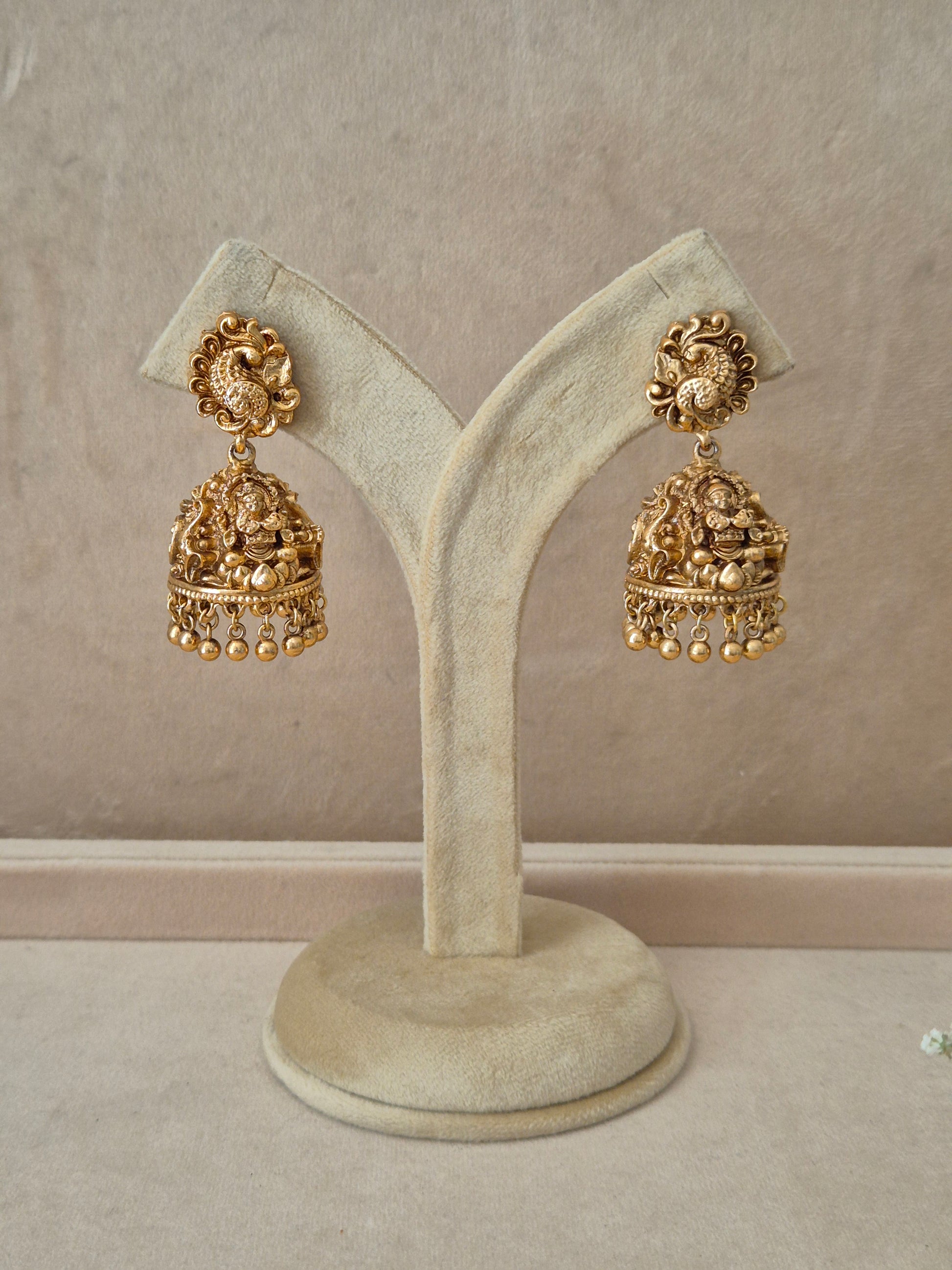 Pair of gold-plated Ishita dangle earrings hanging on a beige velvet display stand, featuring circular studs densely clustered with small white seed pearls and elegant hanging pearl drops by naitri.in