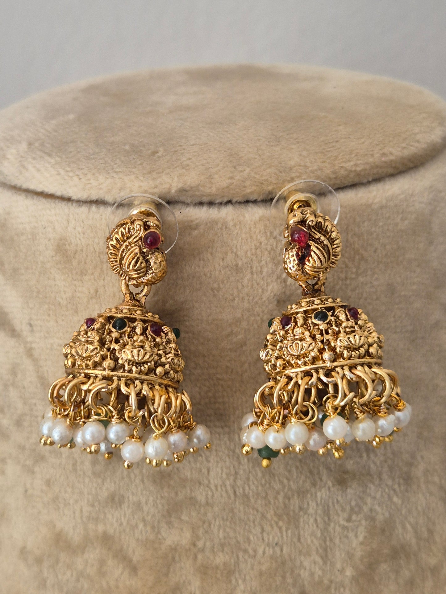 A pair of ornate gold-toned Indian jhumka earrings with white pearl bead borders and small red and green stone accents, by naitri.in