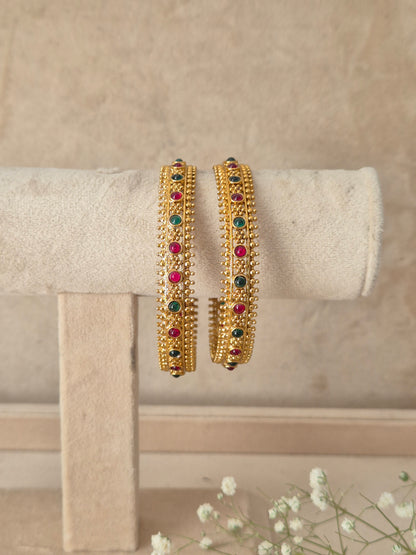 Two gold-plated traditional Indian bangles decorated with small red and green stones, Traditional Indian ethnic bangles adorned with multicolor gemstones and vintage-style gold craftsmanship by naitri.in