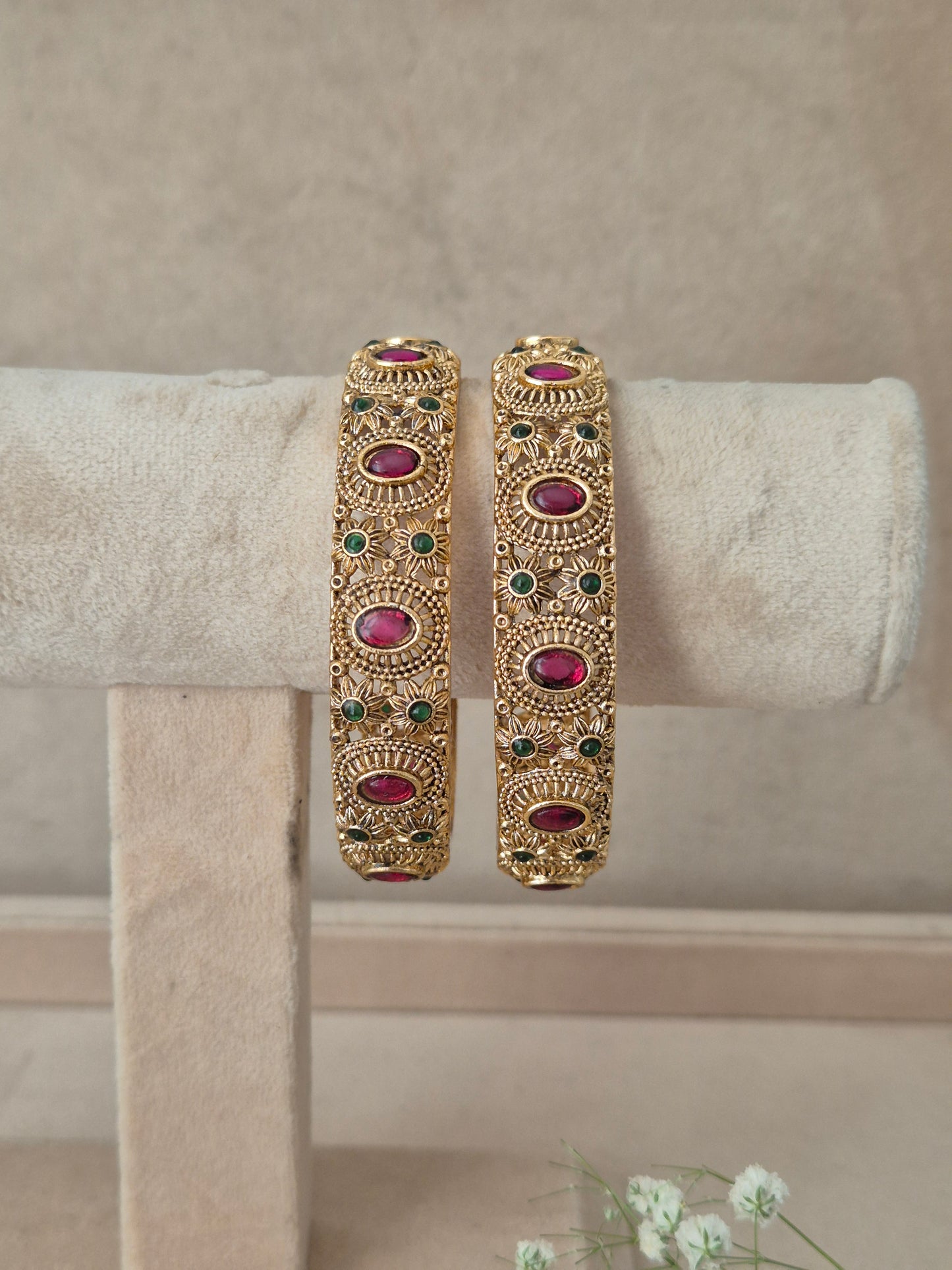 Pair of traditional Indian gold bangles with textured craftwork and embedded ruby-red and emerald-green gemstones, by naitri.in