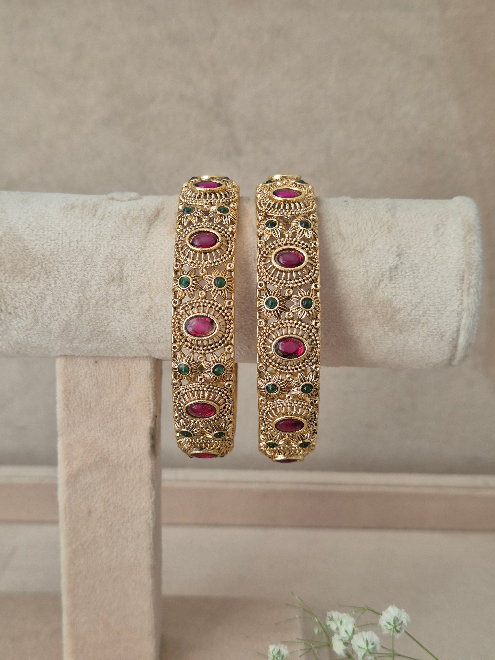 Pair of traditional Indian gold bangles with textured craftwork and embedded ruby-red and emerald-green gemstones, by naitri.in