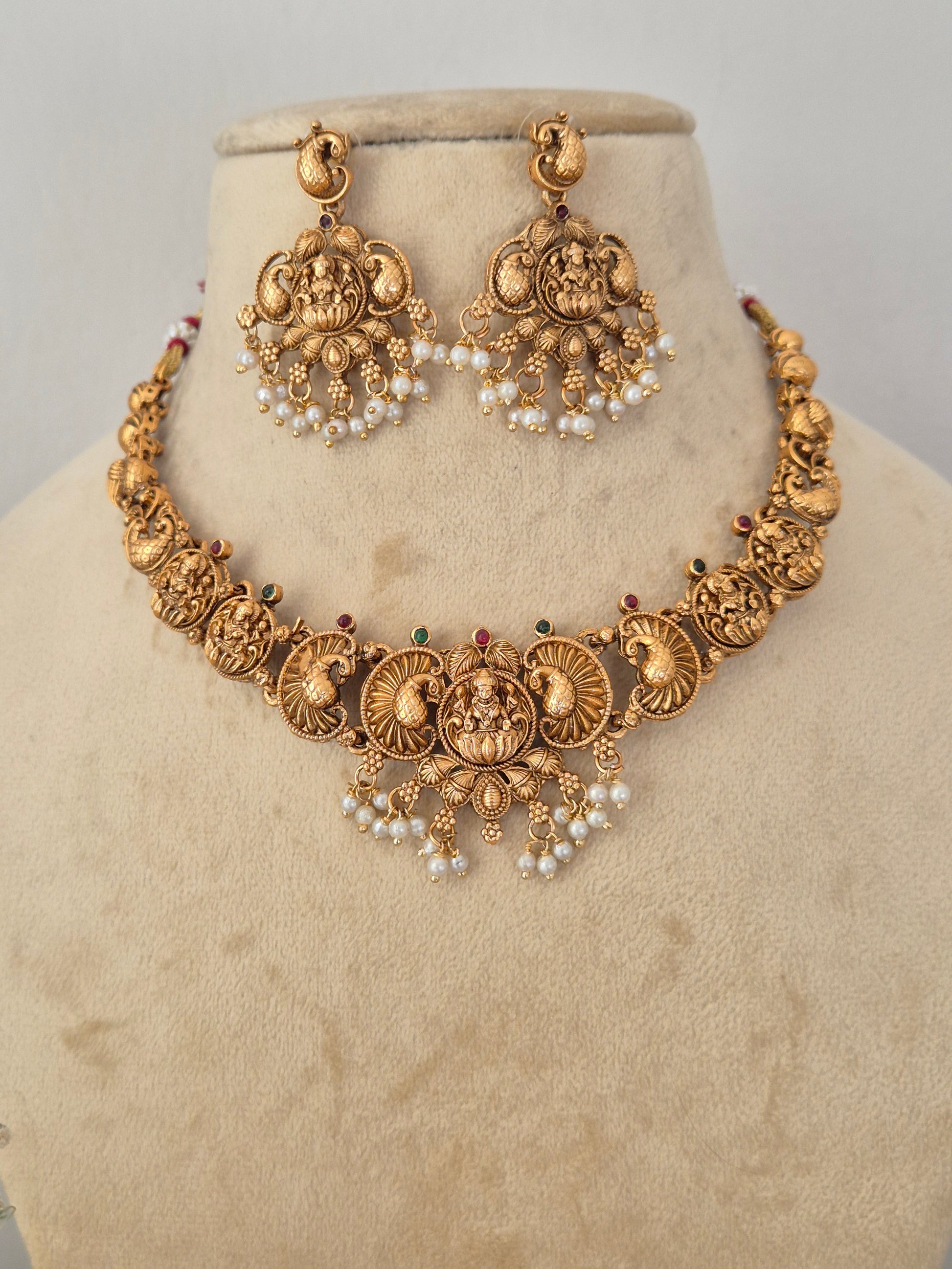 Gold-toned traditional Indian jewelry set featuring a choker necklace and matching earrings with intricate filigree work, floral motifs, and pearl bead clusters, by naitri.in
