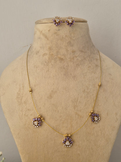 Modern Indian style delicate golden brass alloy necklace and earring set with purple stone embellishments from the NAITRI Jasmeet collection Handcrafted delicate gold chain choker set showcasing geometric crystal and purple stone floral drops by naitri.in