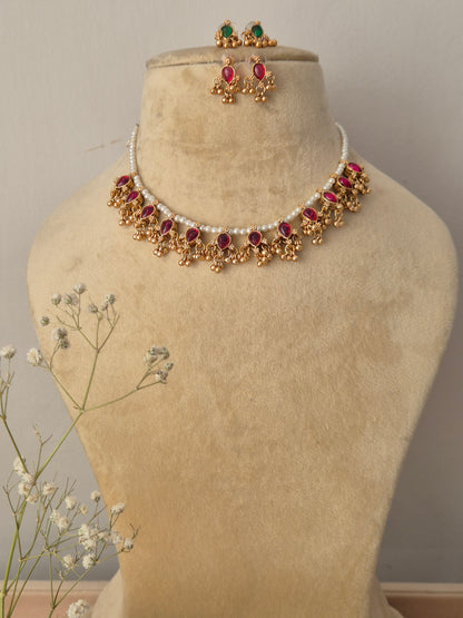 Handcrafted choker necklace featuring a single white pearl strand, a row of ruby-red kemp stones, and a delicate gold bead fringe, displayed with two pairs of matching red and green stud earrings by naitri.in
