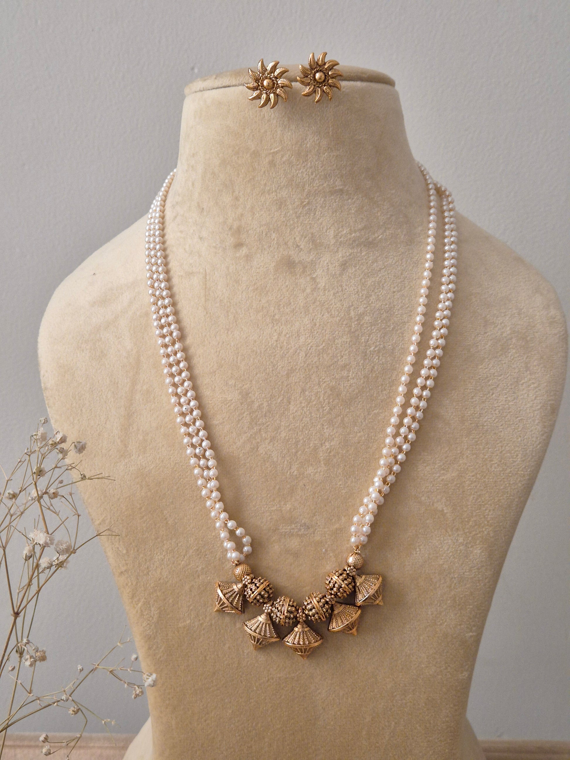 et featuring a multi-strand white pearl necklace with five gold-toned textured jhumka pendants and matching floral stud earrings by naitri.in
