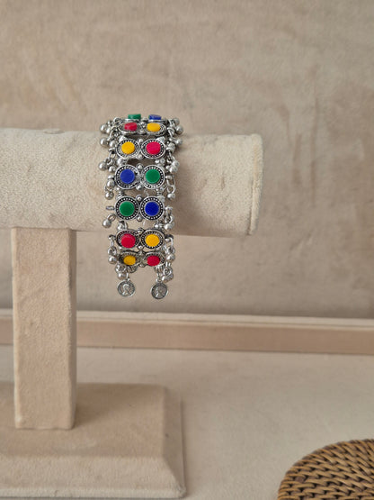 Oxidized silver Jharna bangle bracelet featuring vertical rows of vibrant multi-colored enamel circular charms in red, green, blue, and yellow, detailed with filigree borders and dangling silver ghungroo beads by naitri.in