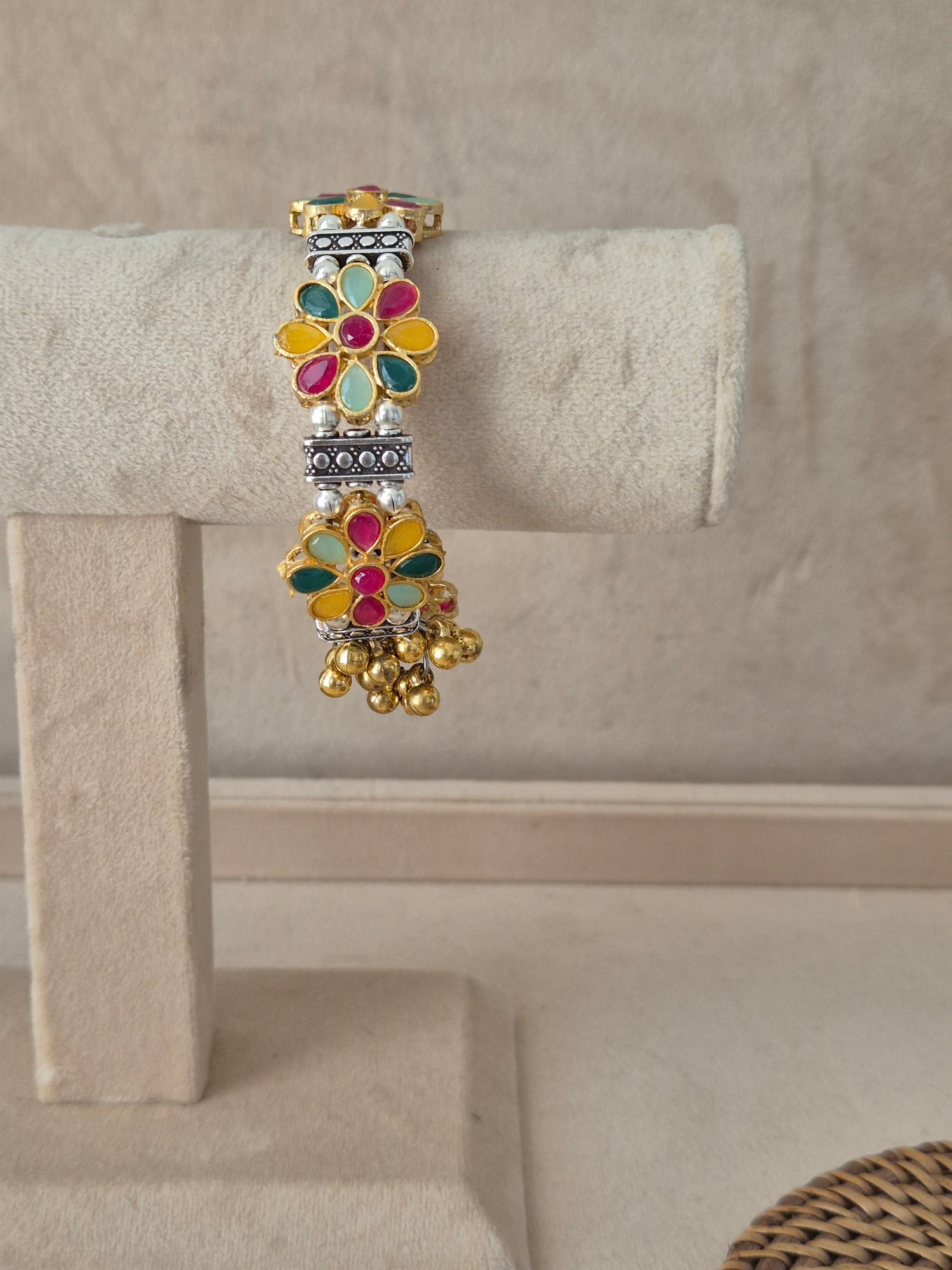Jigesha bangle bracelet featuring multi-colored floral enamel motifs in pink, green, and yellow with light blue accents, flanked by oxidized silver textured spacers and dangling gold ghungroo bead clusters by naitri.in