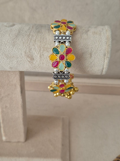 Jigesha bangle with multi-colored enamel flowers and dangling gold ghungroo charms Elegant dual-tone bohemian cuff bracelet with traditional Indian festive detail by naitri.in