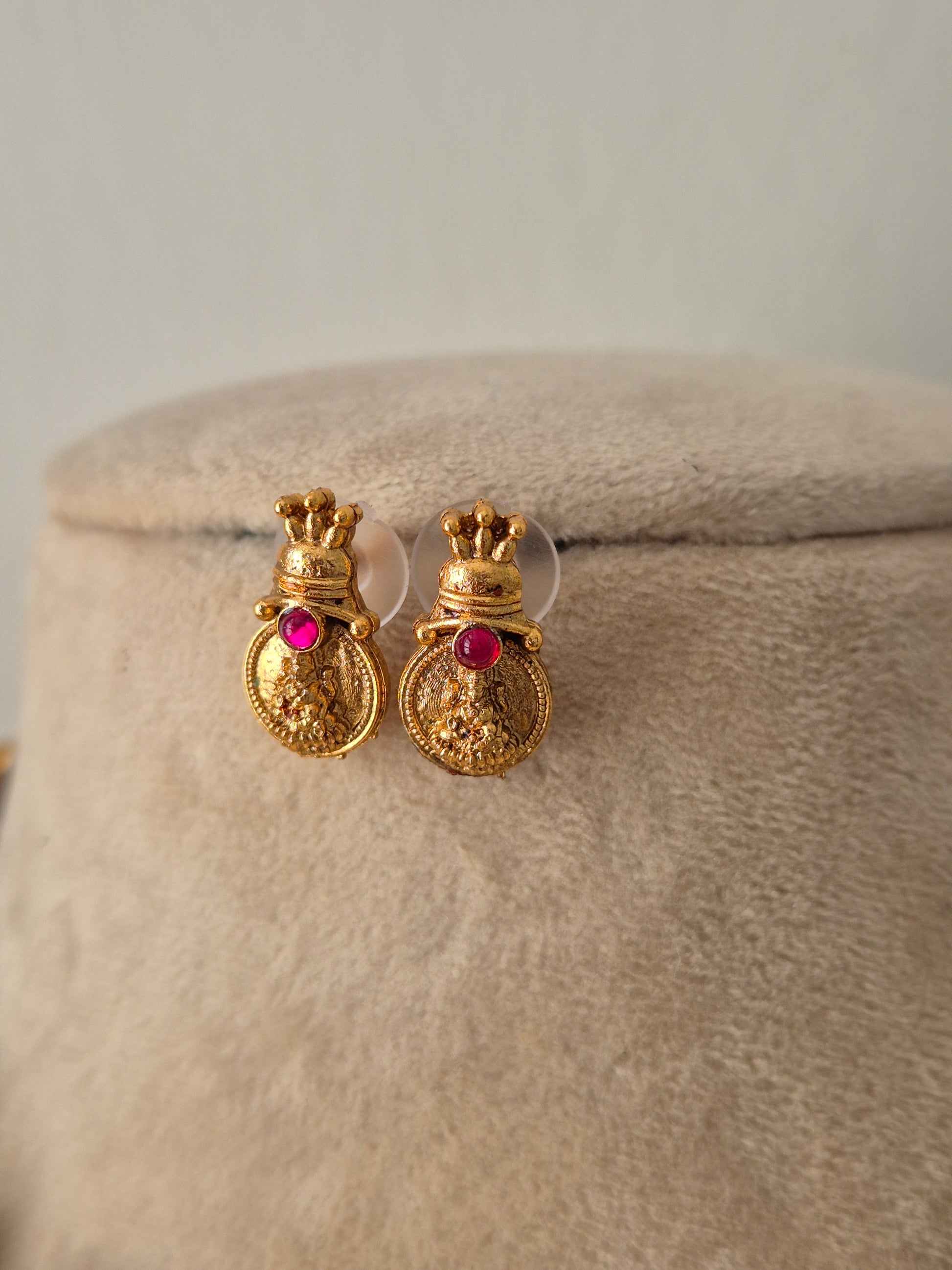 A pair of gold-toned traditional earrings with small red gemstone accents, by naitri.in