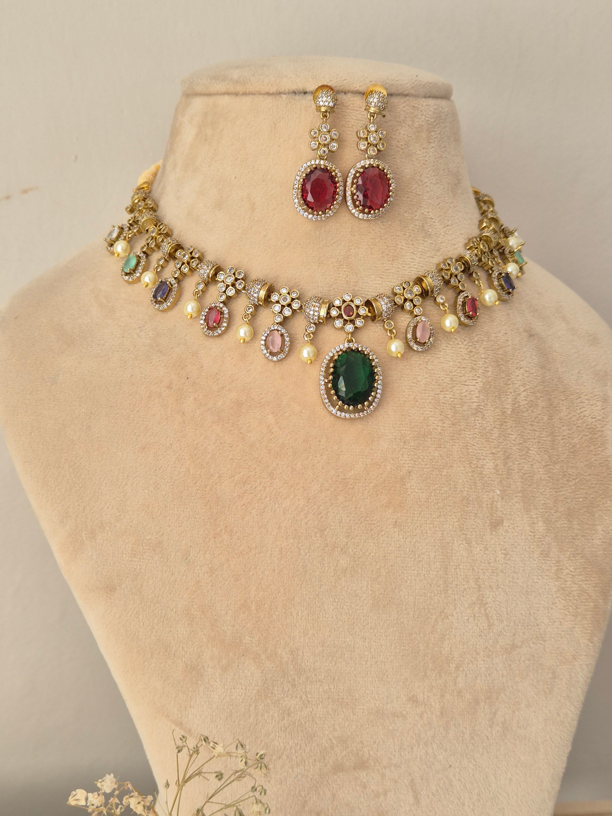 Gold-toned traditional jewelry set, featuring a choker necklace with oval green, red, and pink stones, matching drop earrings, and pearl accents by naitri.in