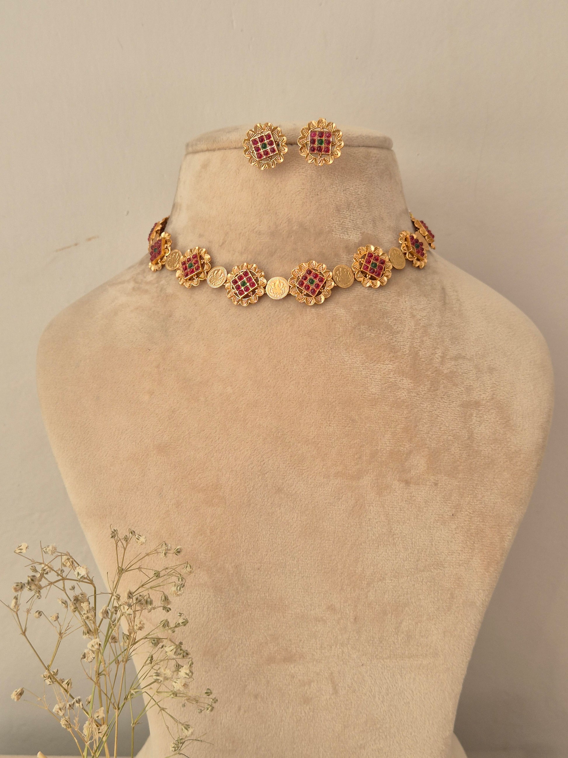 Gold-toned choker necklace and matching stud earrings set with circular floral-patterned motifs inlaid with ruby red and emerald green stones by naitri.in