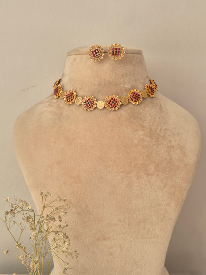 Gold-toned choker necklace and matching stud earrings set with circular floral-patterned motifs inlaid with ruby red and emerald green stones by naitri.in