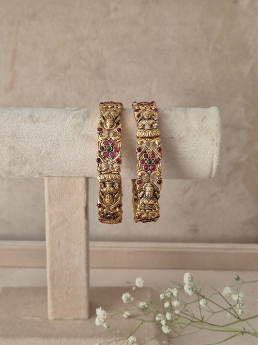 Two ornate gold-toned bangles with detailed filigree and small red gemstone accents, by naitri.in