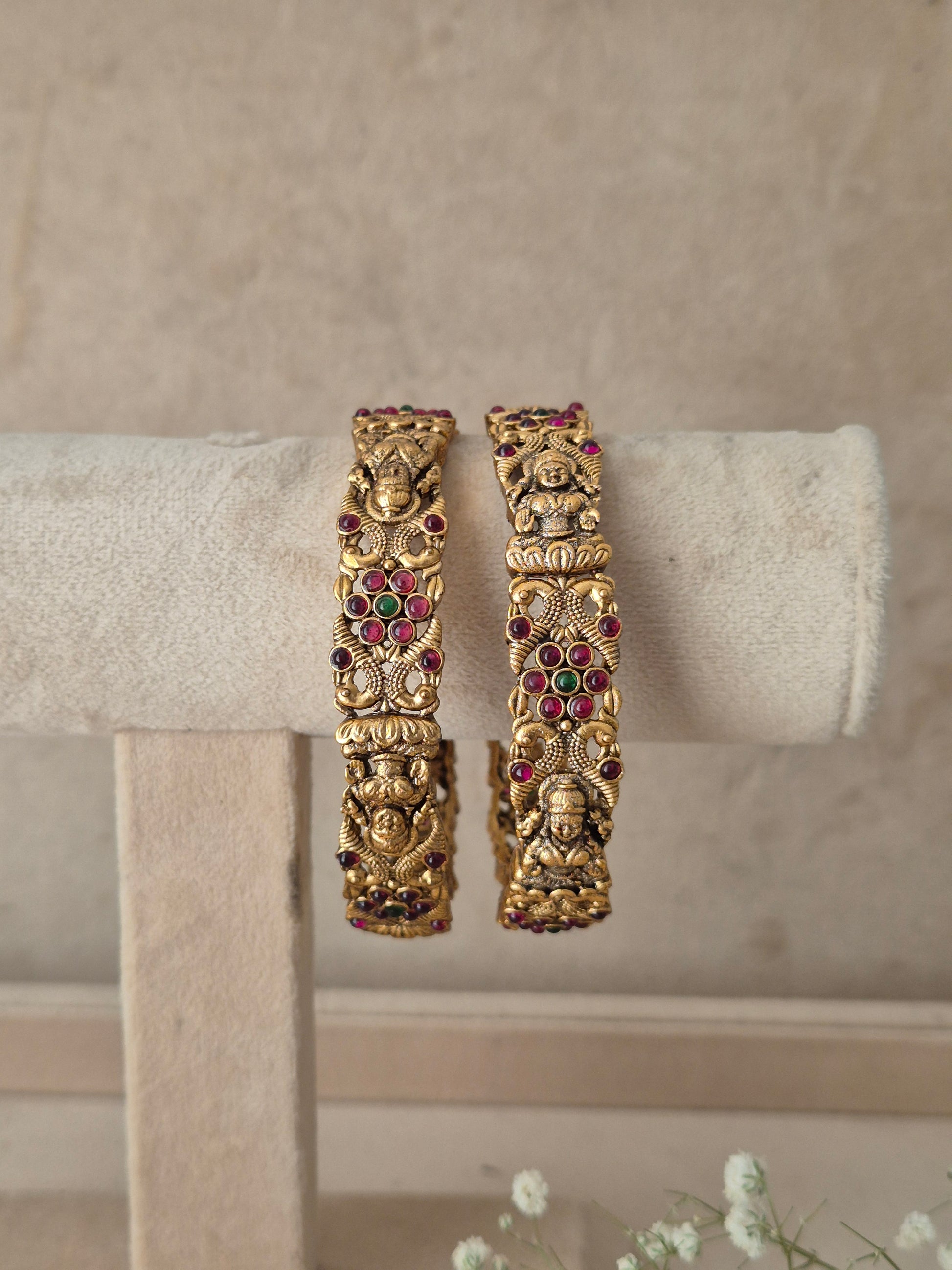 Two gold-toned traditional bangles with detailed filigree and red gemstone accents, by naitri.in