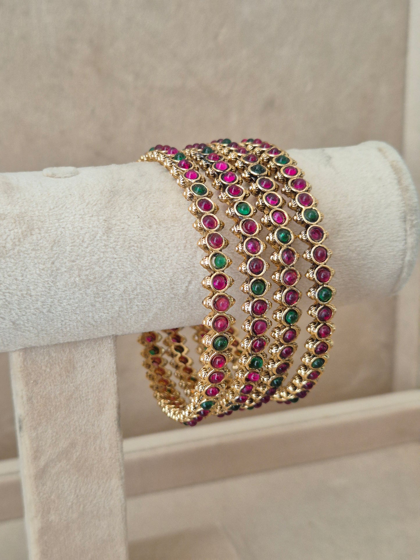Elegant gold statement jewelry set featuring four matching ethnic bangles with vibrant red and green stone details by naitri.in