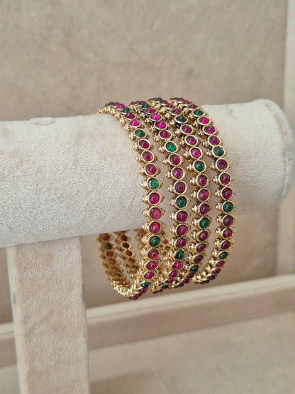 Elegant gold statement jewelry set featuring four matching ethnic bangles with vibrant red and green stone details by naitri.in