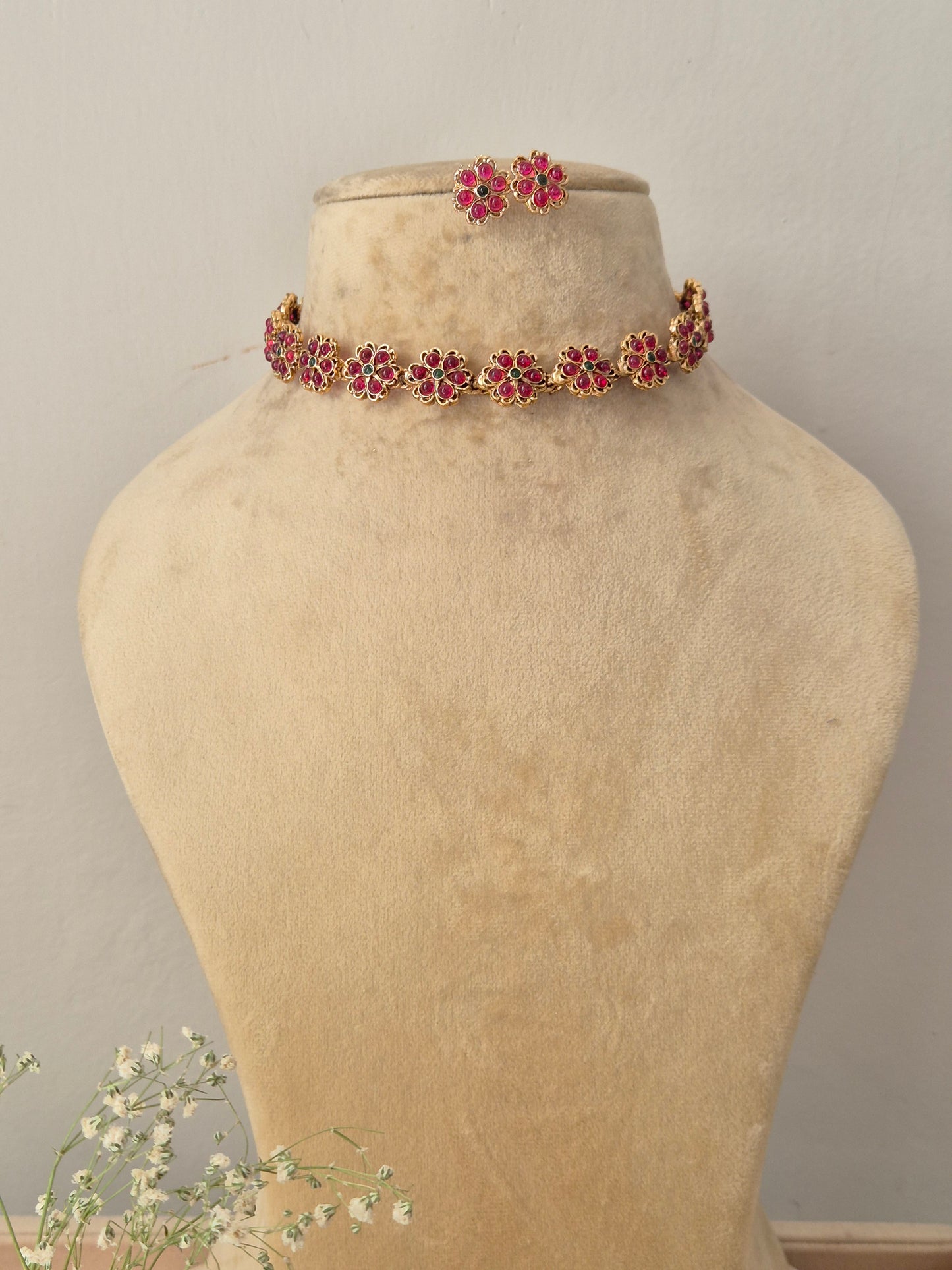 Gold choker necklace featuring a row of pink floral motifs and matching flower stud earrings by naitri.in