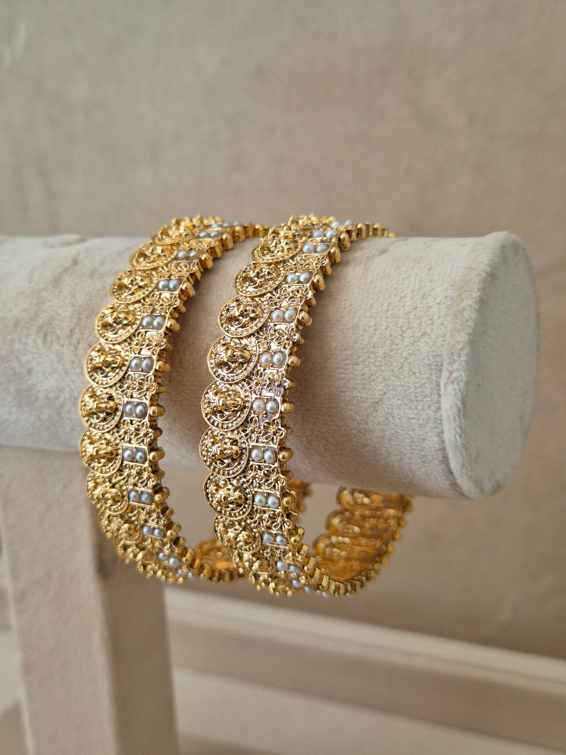 Set of two traditional gold-toned festive bangles with pearl embellishments. by naitri.in