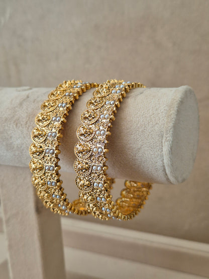 Set of two traditional gold-toned festive bangles with pearl embellishments. by naitri.in