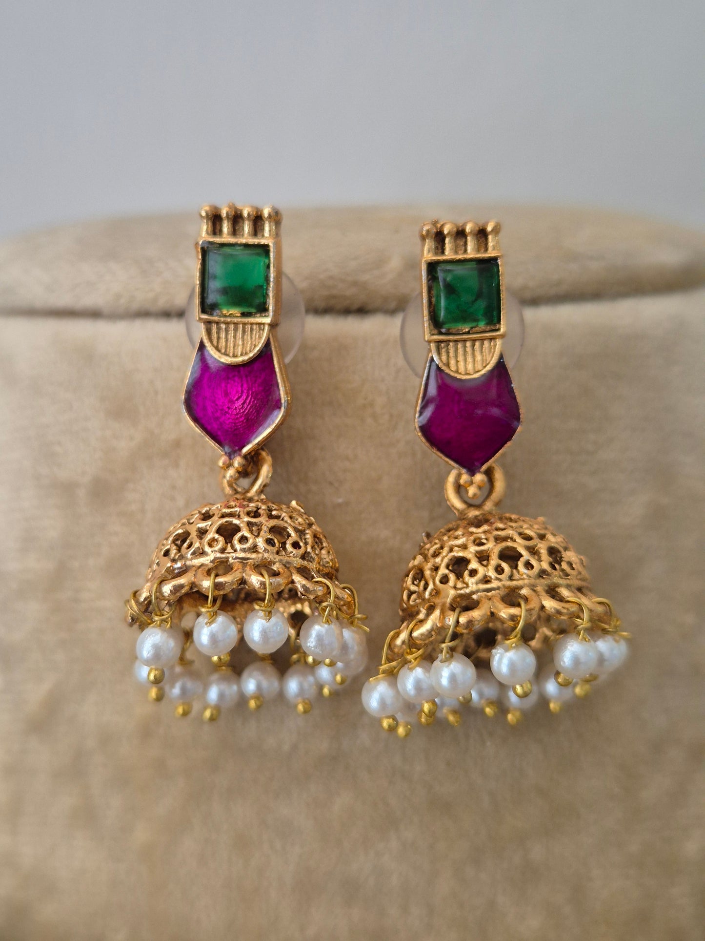 a golden brass alloy earring embedded with vibrant green and pink stones jhumka earrings featuring white pearl drops by naitri.in
