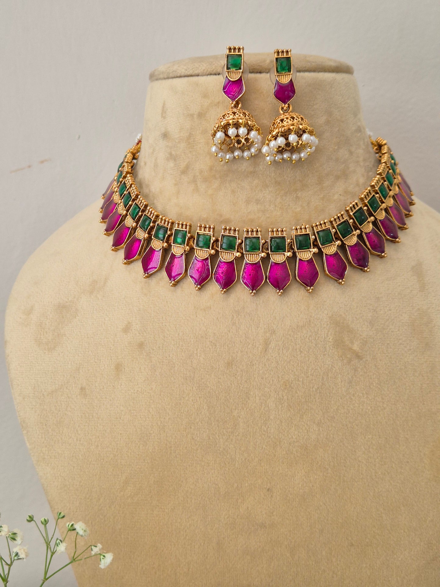 Elegant multi-colored gemstone and gold-toned ethnic choker necklace set, showcased on a minimalist mannequin display next to a sprig of small white flowers by naitri.in