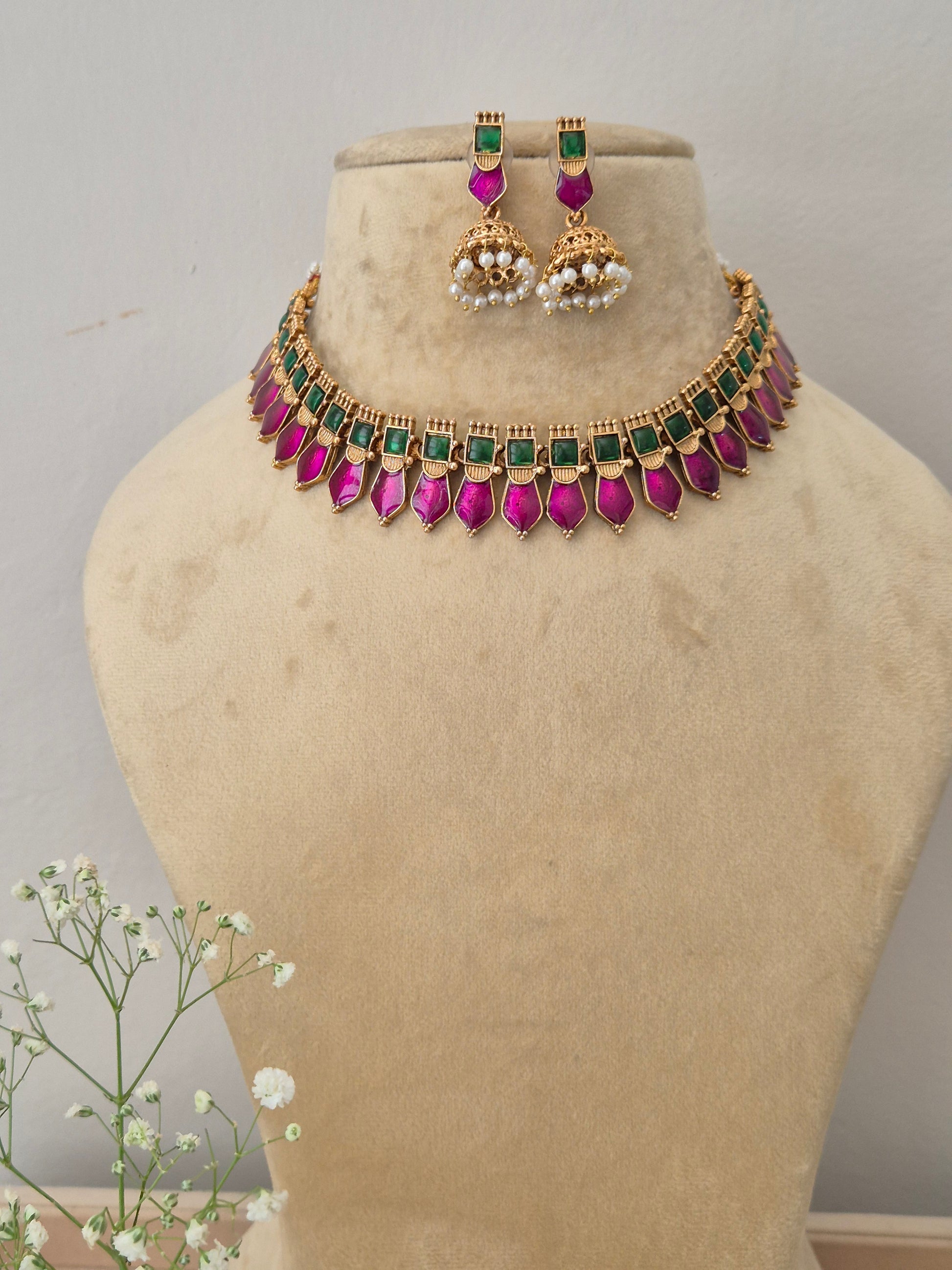 A gold-plated choker necklace featuring a row of square green stones and dangling pink teardrop gemstones, with matching jhumka earrings by naiitri.in