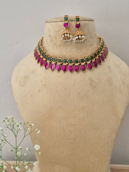 A gold-plated choker necklace featuring a row of square green stones and dangling pink teardrop gemstones, with matching jhumka earrings by naiitri.in