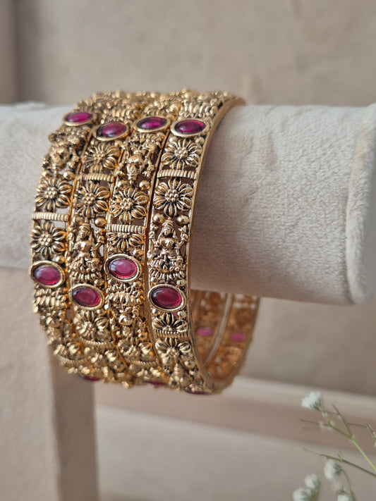 A set of four gold-plated Kashish bangles featuring intricate floral engraving and oval red stone accents by naitri.in
