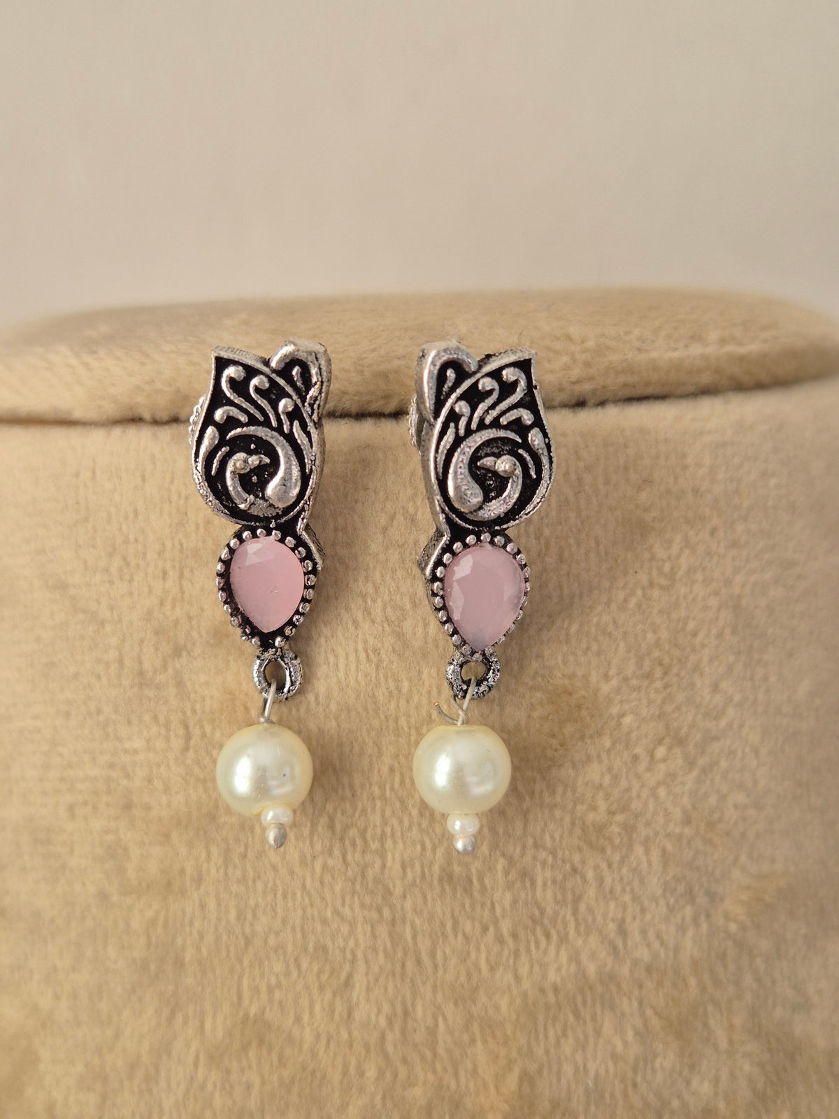 Pair of oxidized silver floral motif earrings featuring light pink stones paired with matching drop pearls by naitri.in