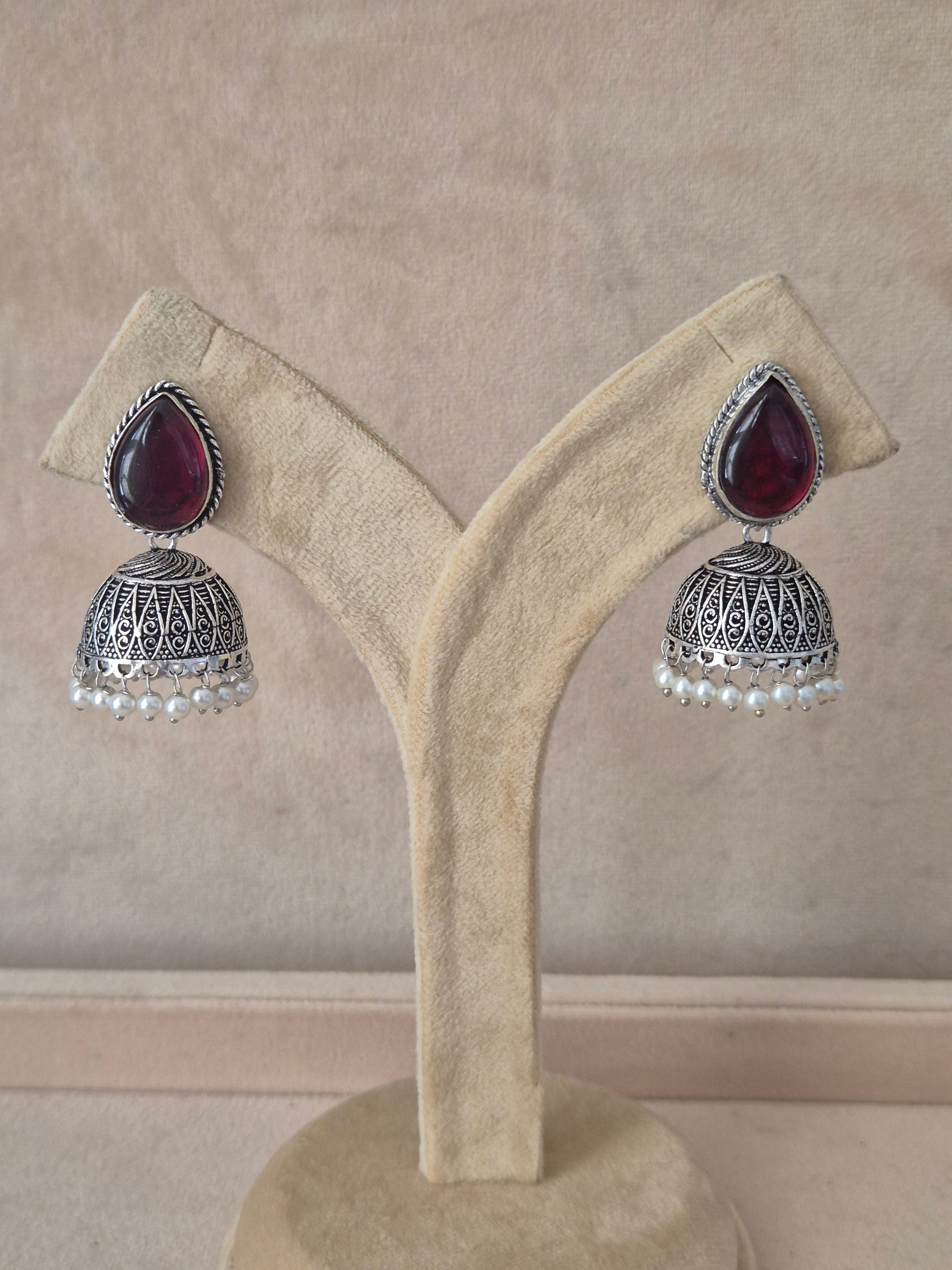 Naitri premium Kasturi oxidized silver jhumka earrings with purple stones from the Silver Jewellery collection. Handcrafted silver oxidized dangle jhumka earrings with dark purple gemstones and small pearl accents by naitri.in