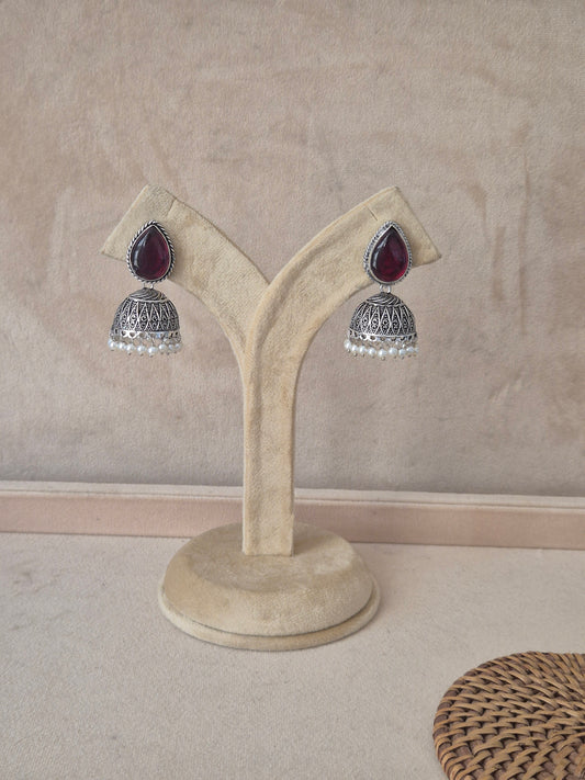Pair of Kasturi silver-toned jhumka earrings featuring tear-drop shaped purple stones and pearl bead drops by naitri.in