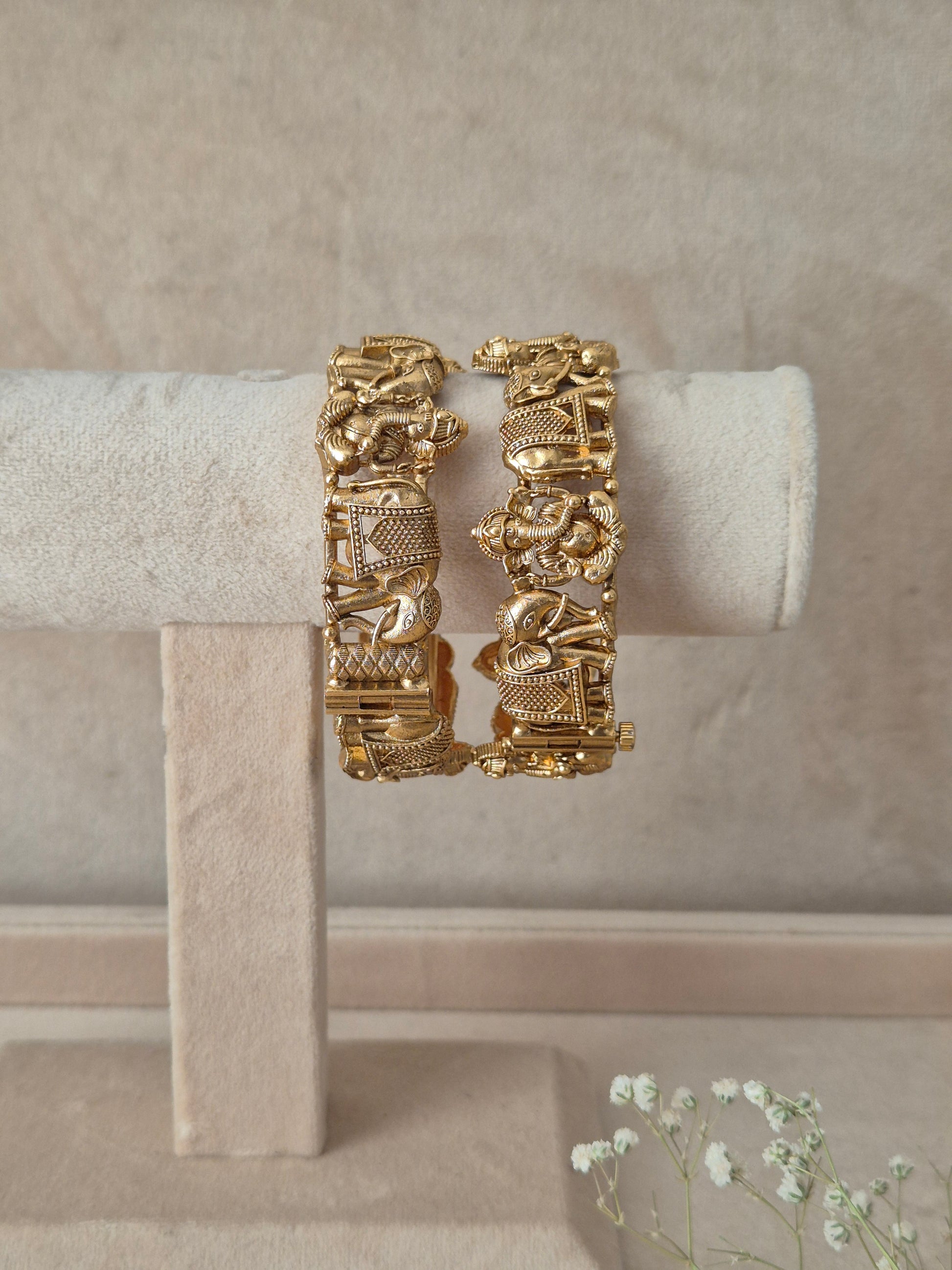 A pair of gold-plated Kavita bangles featuring an intricate embossed elephant motif design with a secure openable clasp, by naitri.in