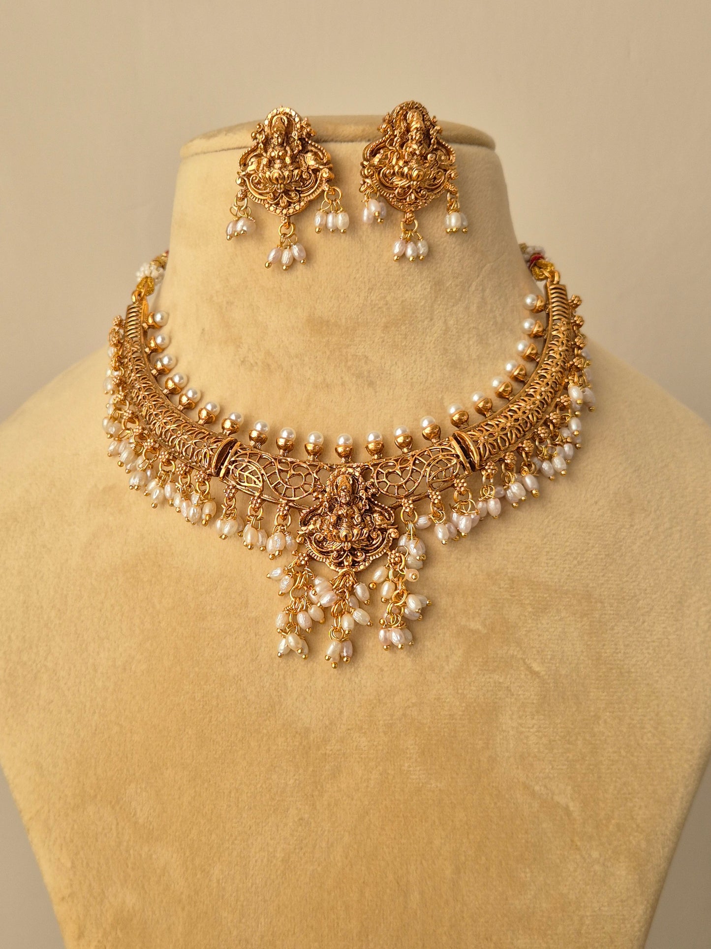featuring a handcrafted golden temple jewellery choker with Goddess Lakshmi motifs, white pearl droplets, and matching jhumka-style earrings by naitri.in