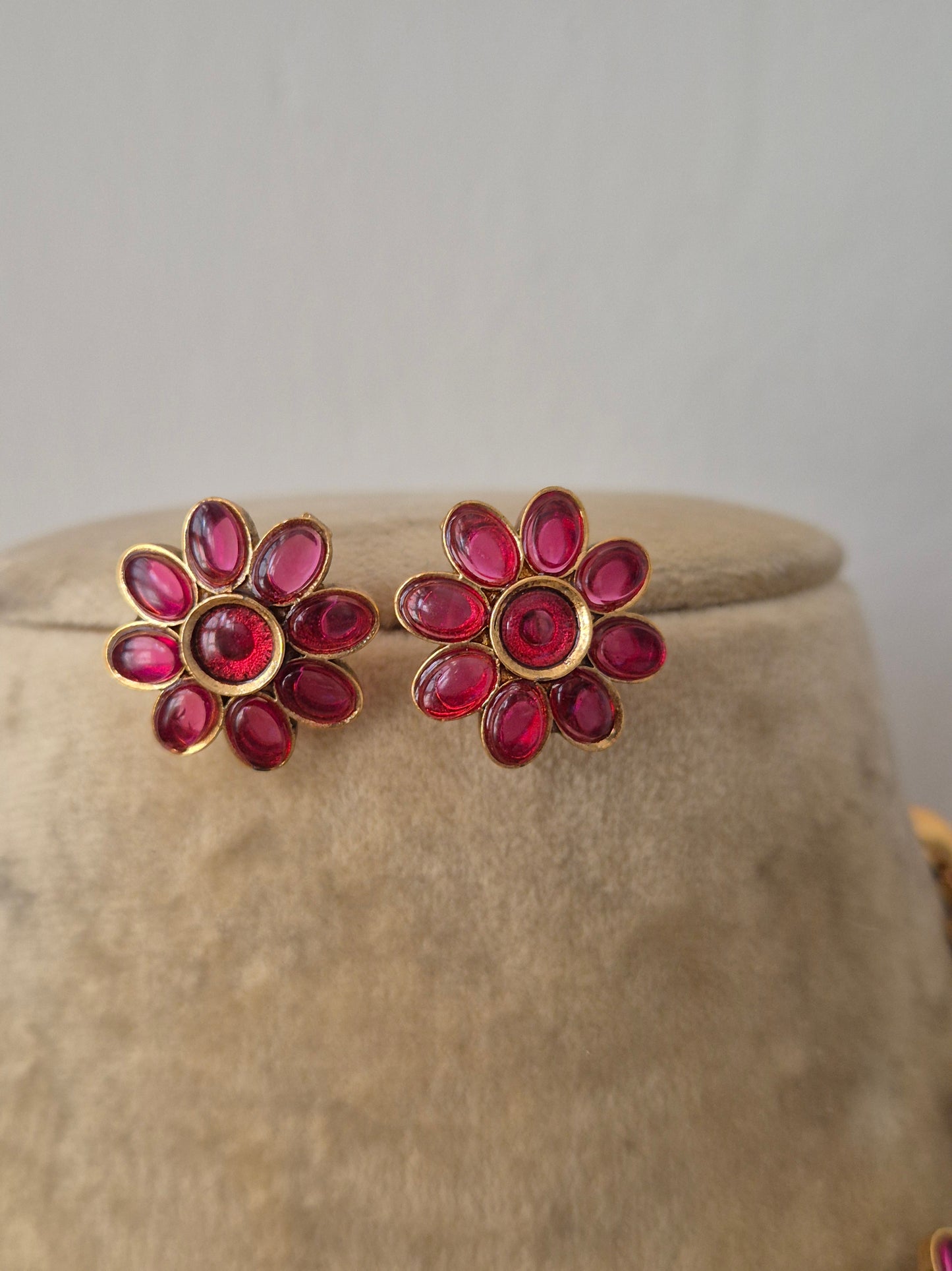 Pair of  earrings embedded with vibrant ruby-red stones in a floral pattern, by naitri.in