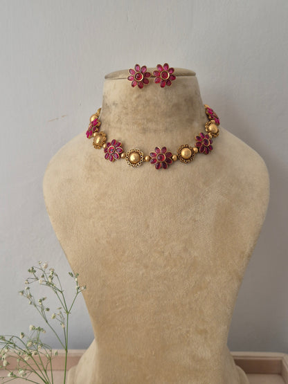 A gold-plated ethnic choker necklace featuring alternating textured round gold charms and red gemstone floral motifs,with matching flower stud earrings by naitri.in