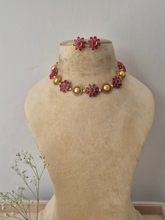 A gold-plated ethnic choker necklace featuring alternating textured round gold charms and red gemstone floral motifs,with matching flower stud earrings by naitri.in