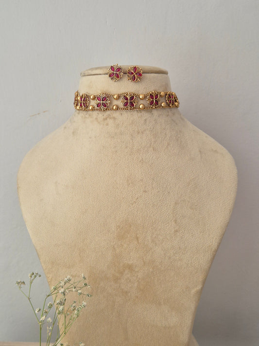 A of gold-toned floral necklace with pink gemstone accents, choker features a continuous row of intricate textured floral motifs inset with vibrant pink gemstones, by naitri.in