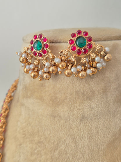 Gold earrings embedded with ruby red and emerald green stones, central circular pendant, and hanging pearl clusters, by naitri.in
