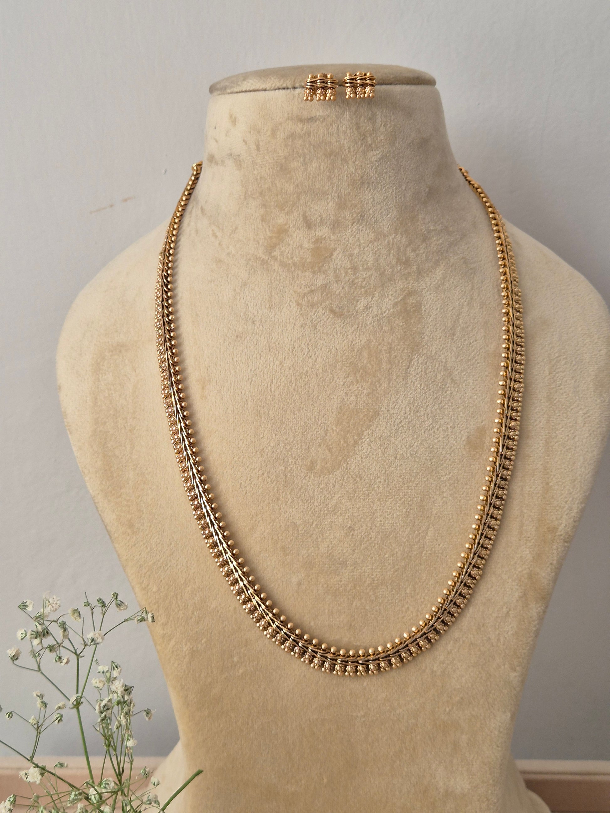 Elegant long gold chain necklace with textured metallic detailing and matching small stud earrings by naitri.in