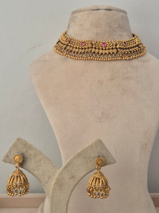Gold-toned traditional jewelry set, featuring a wide choker necklace with small pink stone accents and matching dangling earrings naitri.in